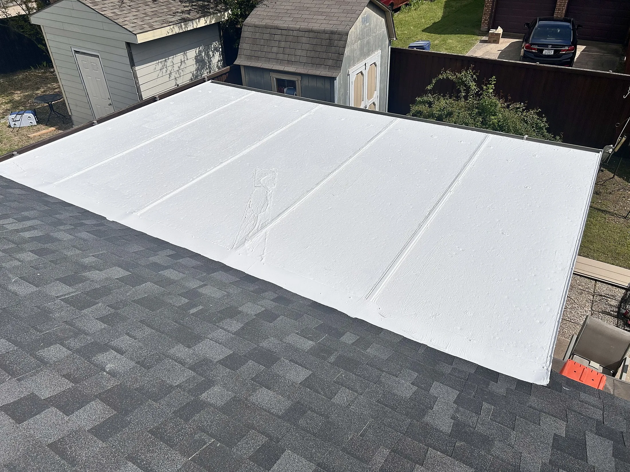 Low-slope roof section finished in white coating beside shingle